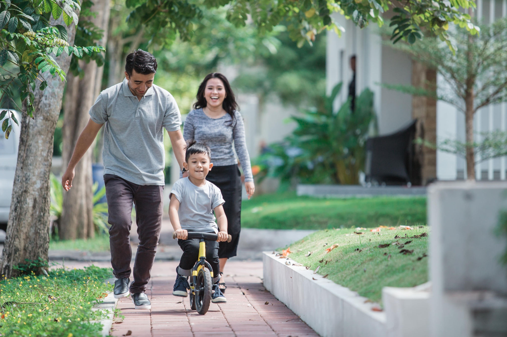 Parents outside with child on push bike learning to ride