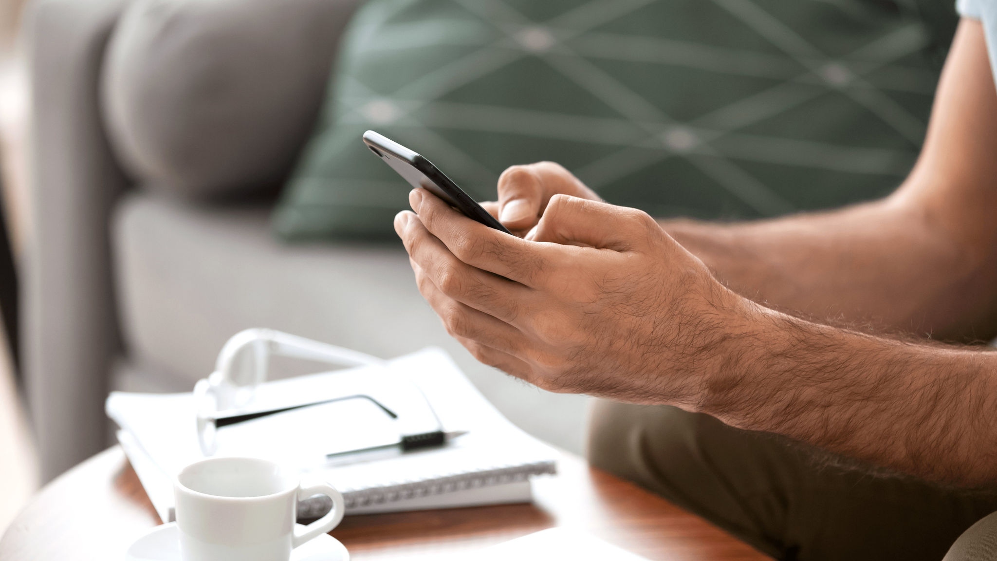 Close up of phone in both hands typing and glasses resting on coffee table