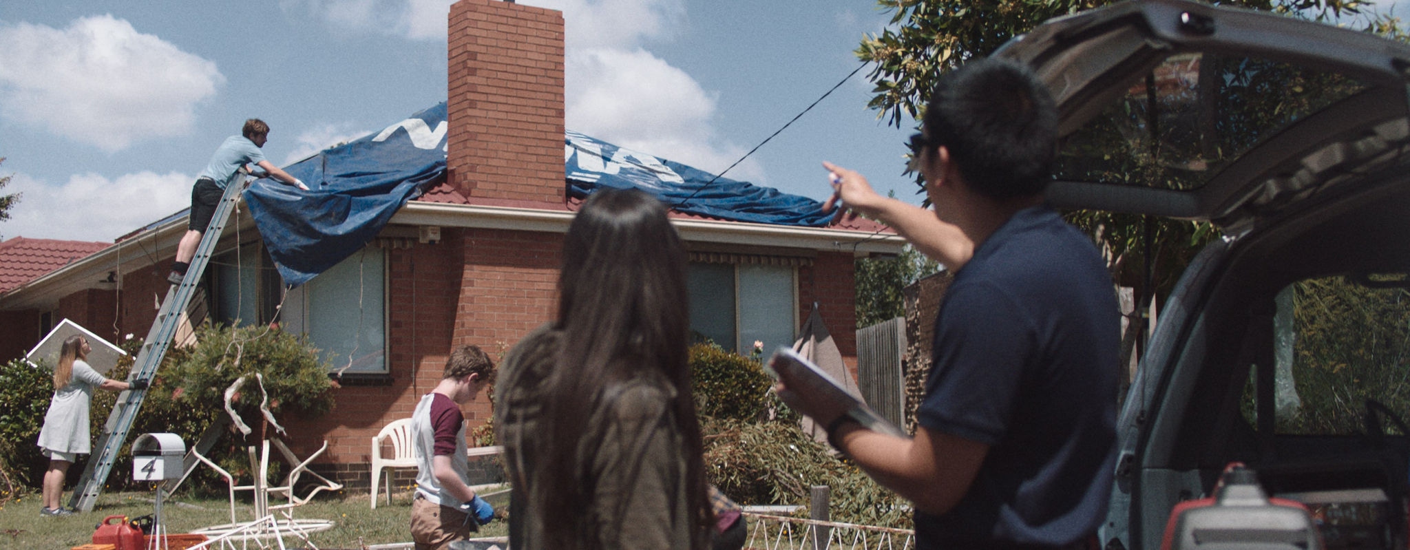 People putting tarp with NRMA logo on roof, claims inspector, talking to customer