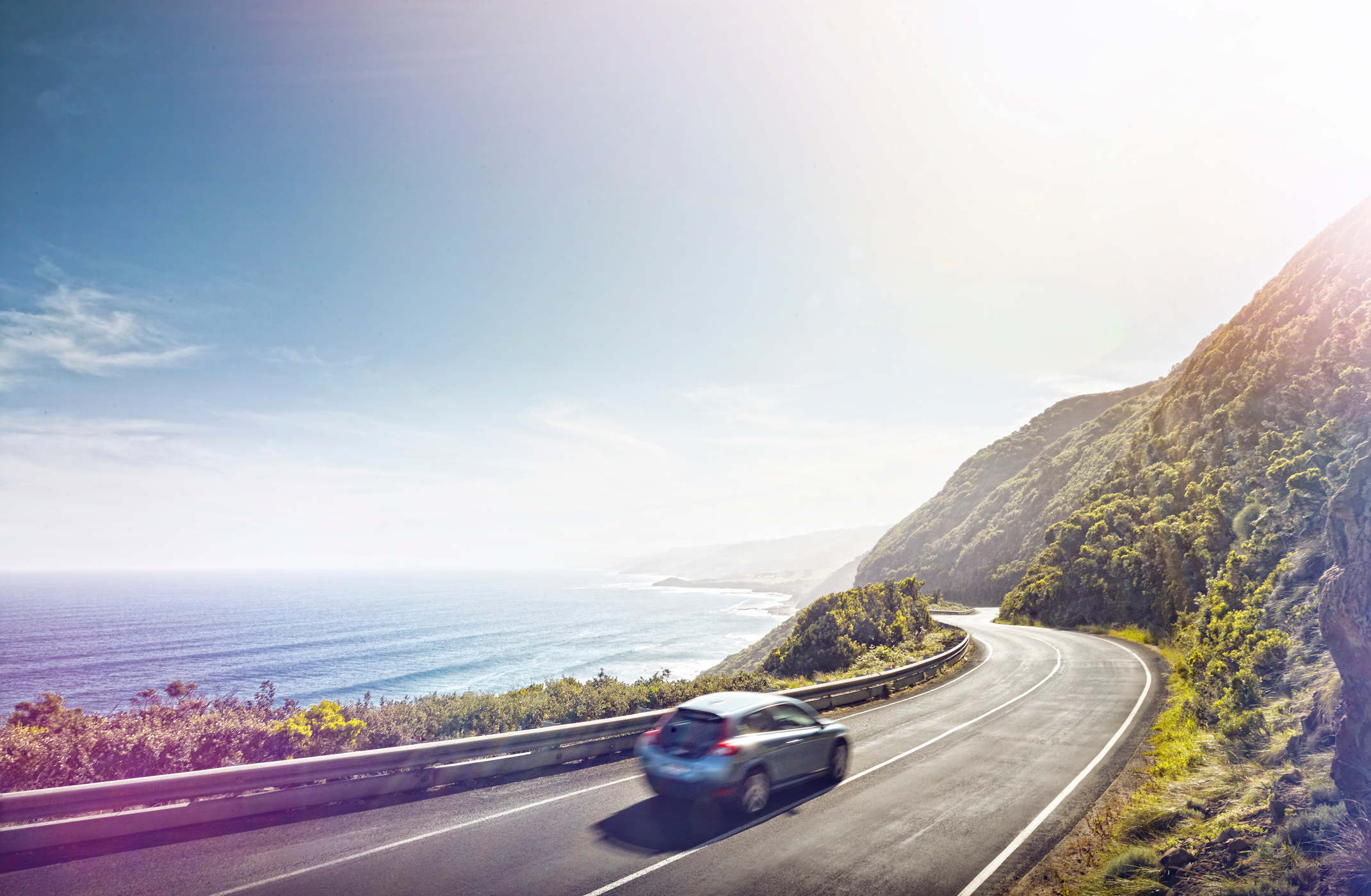 Car driving on a cliff side road ear the ocean