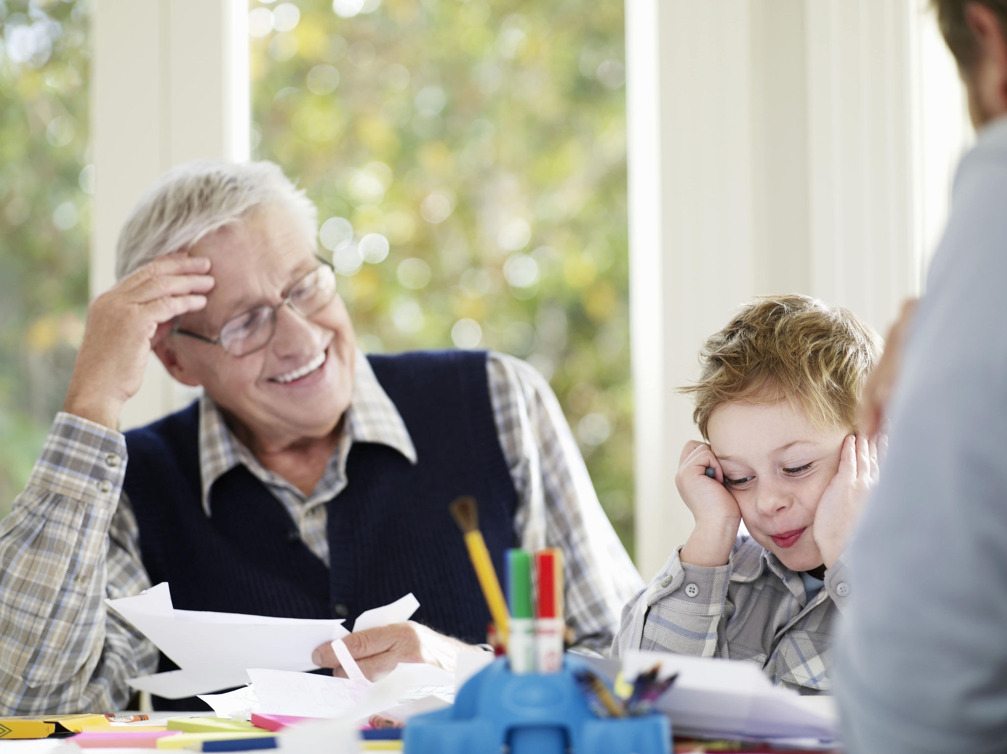 Grandparent and child sitting at table. Child holding grey crayon 