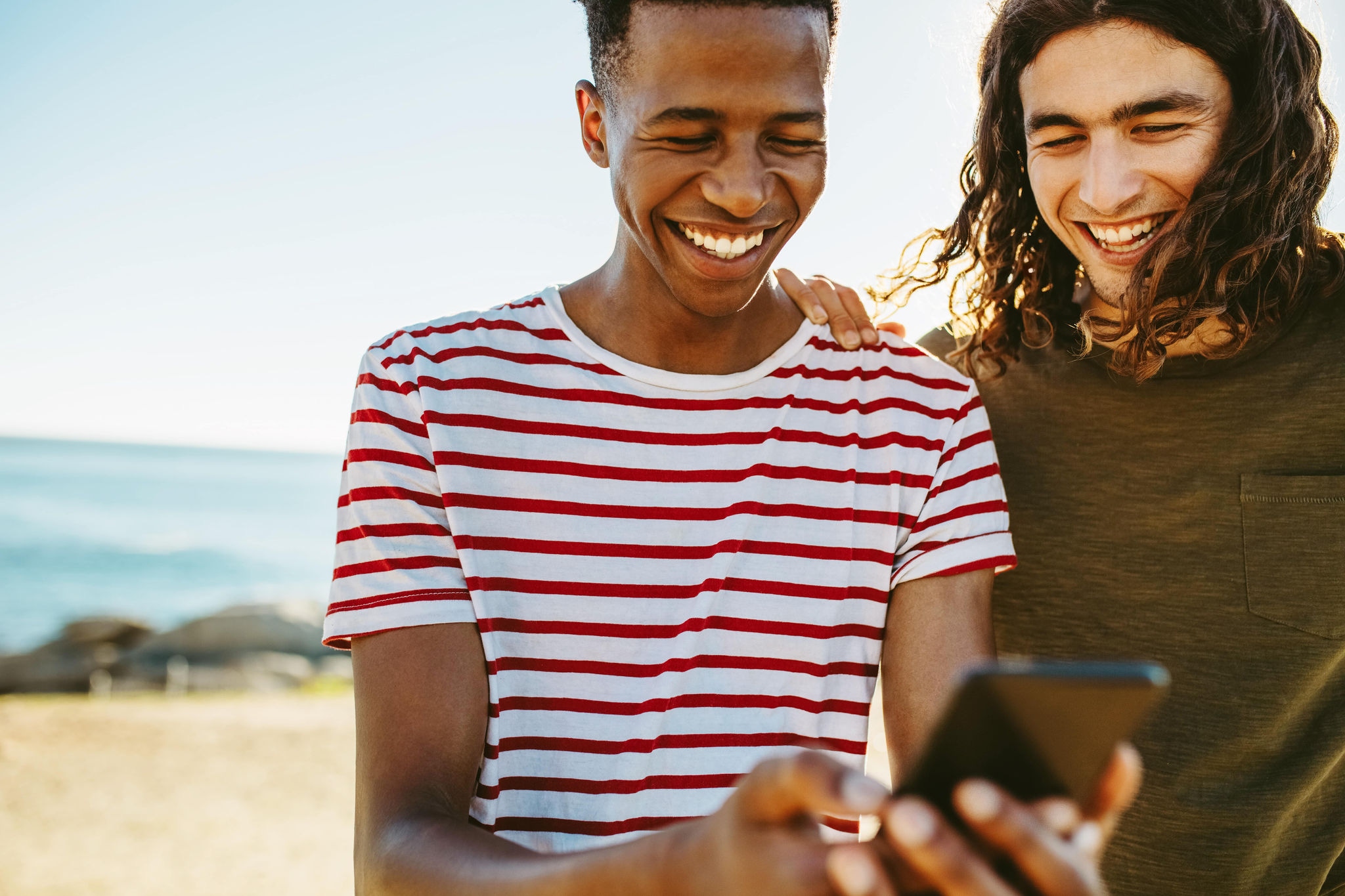 People looking at a phone and laughing at the beach